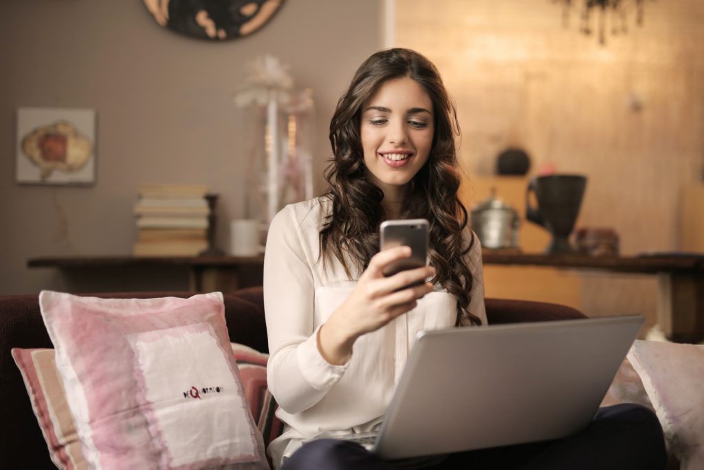 Perempuan tersenyum memegang handphone dan laptop